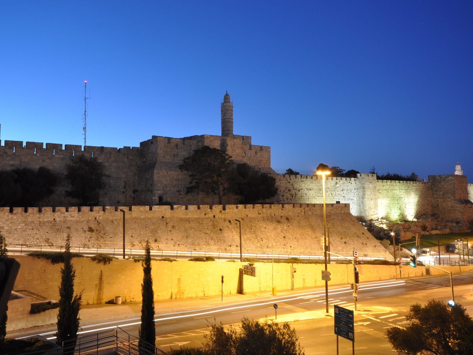 מגדל דוד וחומות העיר העתיקה בירושלים מוארים בשעת דמדומים, מעל הכביש.